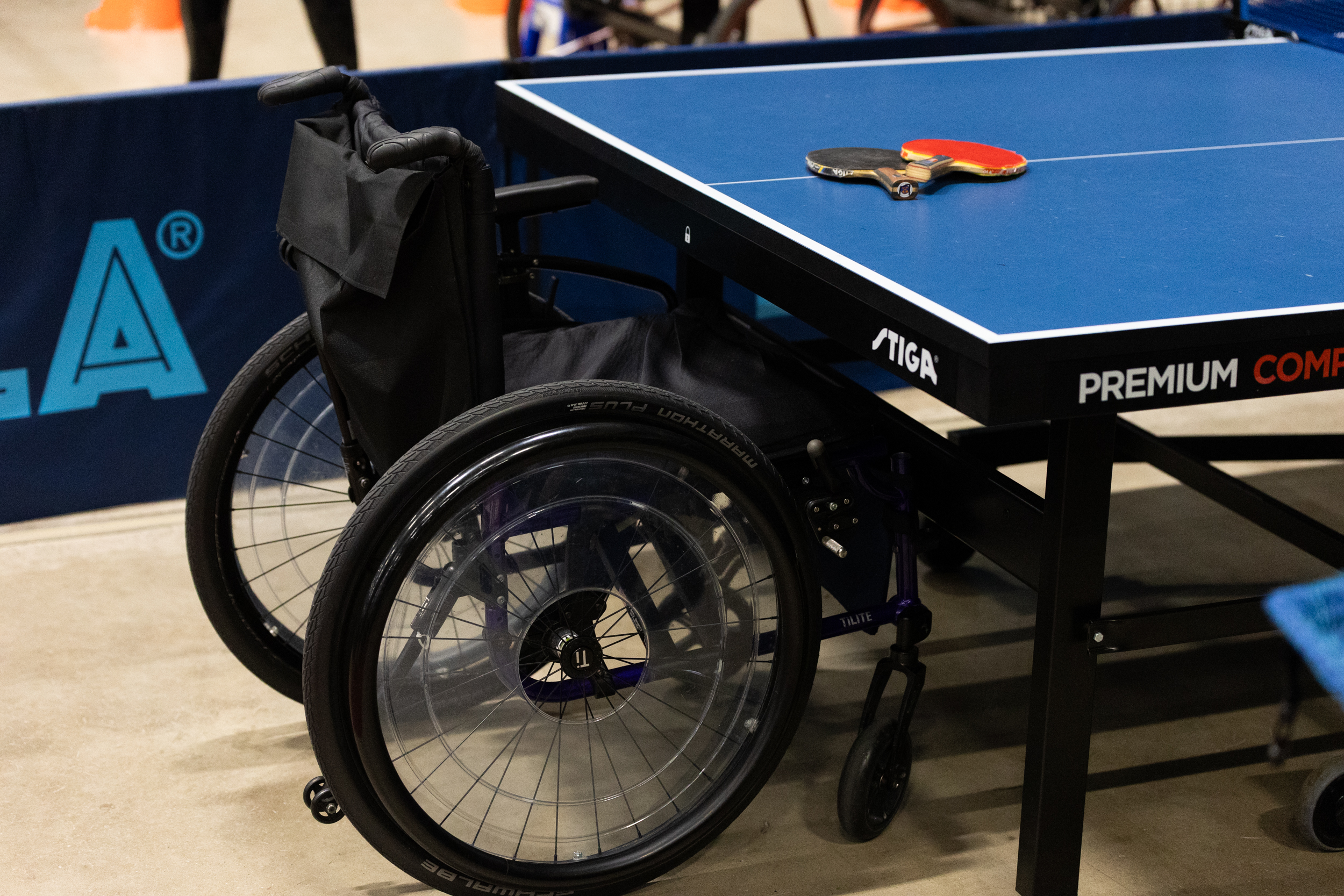 Kuvassa pöytätennispöydän pääty ja päädyssä pyörätuoli